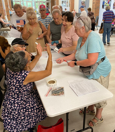 Two volunteers behind a long table greet a group of  seniors who are applying to receive PA farmers' market checks. 