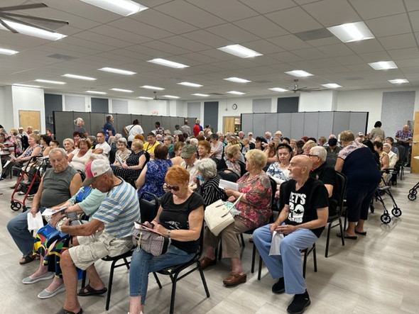 A large group of seniors sit in chairs while waiting to receive PA farmers' market checks. There are 7 rows of 10 chairs with a senior in each chair. 